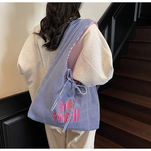Close-up of canvas tote bag with blue stripes and pink be well text on the back