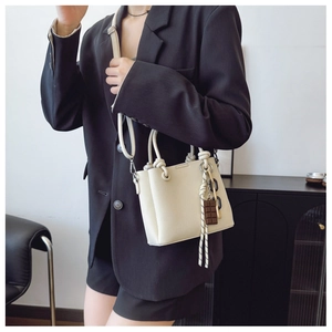 Vue détaillée de la texture litchi blanc crème et du pendentif chocolat sur le sac seau