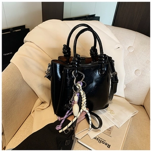 Détail d'un sac seau noir brillant avec des breloques créatives et ferrures en métal