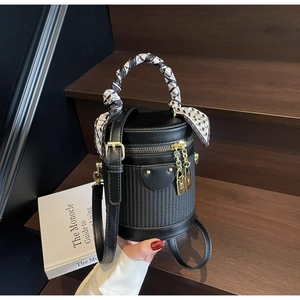 Detailed shot of black cylindrical bucket bag featuring woven texture and silk scarf handle