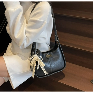 Detail of black hobo bag with embossed texture and elegant pearl lace bow charm
