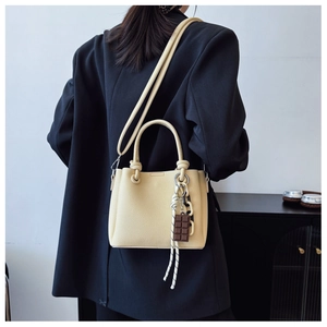 Détail du sac seau en cuir beige avec breloque porté sur une veste de blazer noire