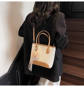 Detail of woven bucket bag with brown leather trim and cute teddy bear charm accessory