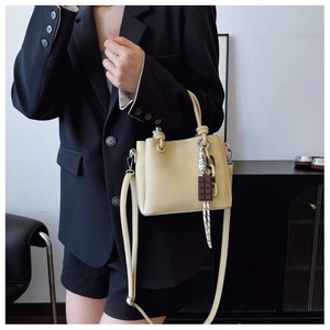 Gros plan du sac seau en cuir crème avec poignée et pendentif en forme de chocolat