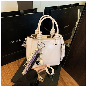 Détail du sac seau beige avec poignée nouée et breloques fantaisie sur la bandoulière