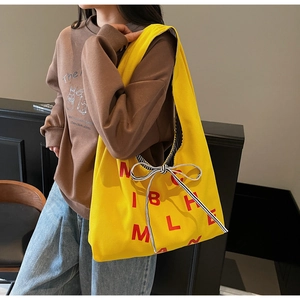 Detail of a large yellow canvas tote bag with red letters and a striped ribbon bow