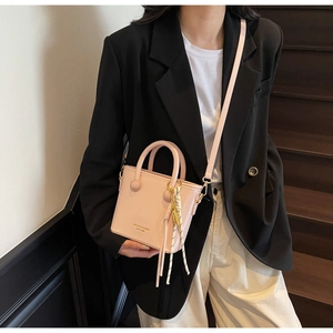 Détail d'un sac seau rose crème avec breloque à pompon et lettrage de marque chic
