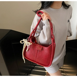 Close-up of red crescent shoulder bag with white pearl woven bow pendant detail