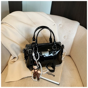Detail of black patent leather Boston bag with silver hardware and a pearl chain charm