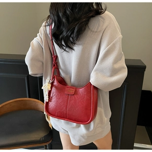 Detail of red pleated underarm bag with pearl butterfly charm and brand logo patch