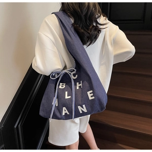 Detail of navy blue denim tote bag with white lettering and striped ribbon bow decoration