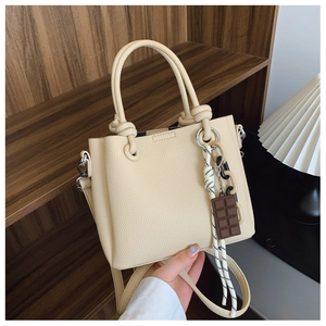 Gros plan du sac seau en cuir beige avec poignée nouée et breloques de sac élégantes
