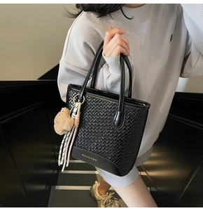 Close-up of black woven leather bucket bag with gold logo and stylish scarf charm