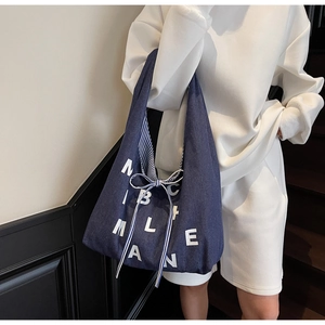 Detail of navy blue tote bag featuring white letter prints and striped bow tie strap