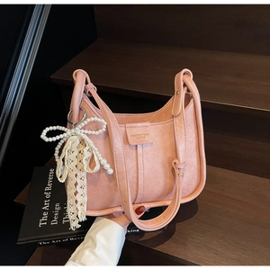 Detail of pink leather underarm bag featuring pearl bow and lace pendant on wood steps
