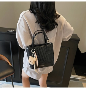 Detail of black woven tote bag with plush bear charm and tassel on a female model