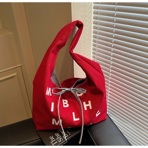 Detail of red canvas tote bag showing white letter print and decorative striped bow ribbon