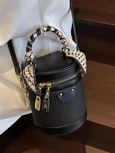 Elegant black barrel bag with woven texture, gold zipper, and silk scarf handle detail