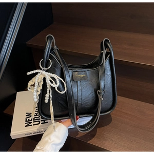 Detail of a black textured leather tote bag with a pearl lace bow charm on stairs