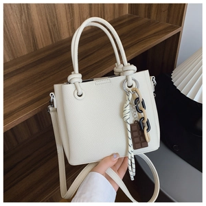 Détail d'un sac seau crème avec texture litchi, anse nouée et breloques décoratives
