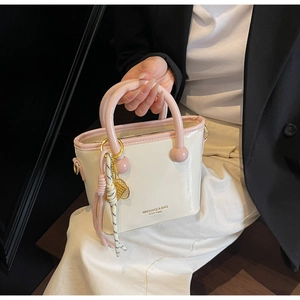 Détail d'un sac seau blanc crème avec bords roses et pendentif en métal tenu par un modèle