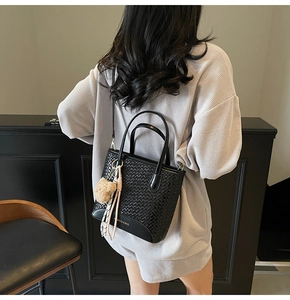 Detail of black woven leather tote bag with bear charm and silk scarf on gray outfit
