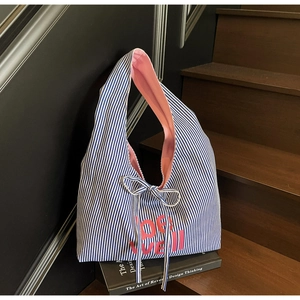 Detail of blue striped tote bag featuring pink lining and a decorative ribbon bow