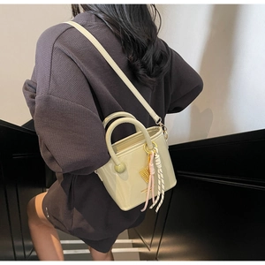Vue latérale détaillée du sac seau crème avec bandoulière et pendentif à pompon décoratif