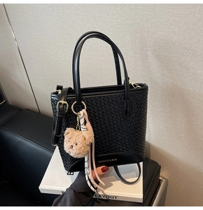 Close-up of black woven leather bucket bag with plush bear charm and braided rope detail