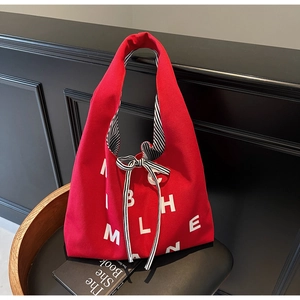 Detail of red canvas tote bag with letter print and decorative black-white striped bow