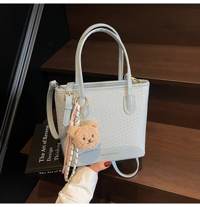 Detail of light blue woven leather bucket bag with cute bear charm on wooden steps