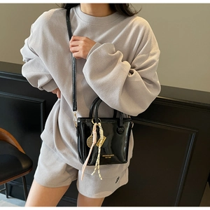 Détail du sac seau en cuir verni noir avec logo doré et pendentif de raquette de tennis