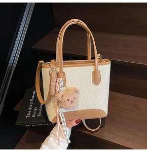 Detail of woven white texture and brown leather trim on tote bag with a plush bear charm