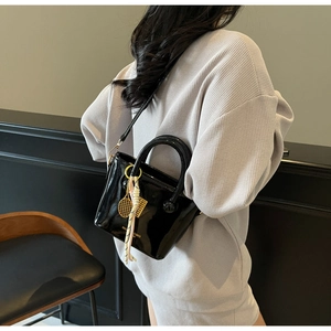 Détail d'un sac seau en cuir verni noir brillant avec breloques dorées de tennis