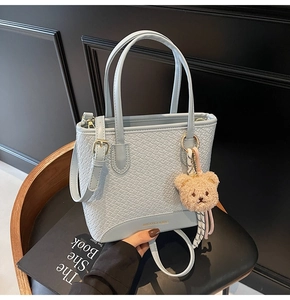 Detail showing woven texture of blue bucket bag with plush bear charm and gold hardware