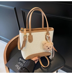 Detail of woven texture tote bag with brown leather trim and cute plush bear charm accessory