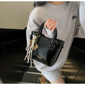 Détail du sac seau en cuir verni noir avec breloques dorées et ruban élégant