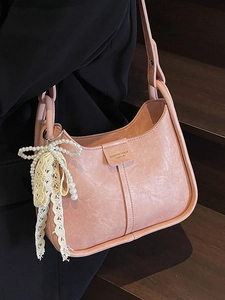 Pink faux leather underarm bag with a pearl and lace bow charm on black attire