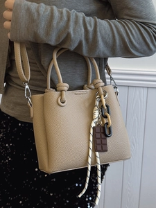 Sac seau beige minimaliste avec poignée à nœud et chaîne en résine porté par un mannequin