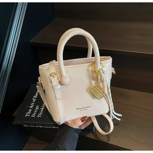 Détail d'un sac seau en cuir verni rose crème avec ferrures dorées et pompon décoratif