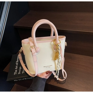 Détail du sac seau crème avec accents roses posé sur des marches en bois