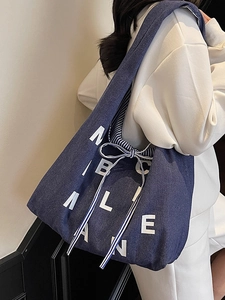 Blue denim tote bag with white letter print and striped bow detail shown on a model