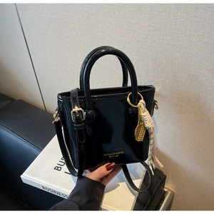 Détail du sac seau en cuir verni noir brillant avec logo doré et pendentif de raquette