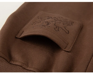 Close-up of thick brown cotton fleece fabric with detailed lion embroidery on the pocket
