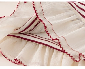 Macro shot of layered cream tulle fabric with red wavy stitched edges and striped lining