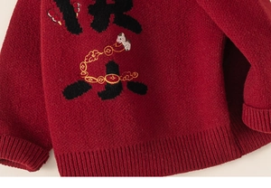 Detail of red knitted kids sweater featuring embroidered dragon and festive characters