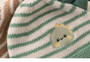 Detail of green and white striped knit baby hat featuring a cute dinosaur embroidery patch