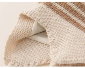 Close-up of beige knit baby hat fabric showing soft wool texture and striped pattern detail