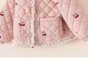 Détail de la veste en coton matelassé rose avec broderie cerise et jolis nœuds