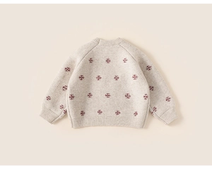 Detailed view of cream knit sweater featuring red snowflake patterns and ribbed cuffs